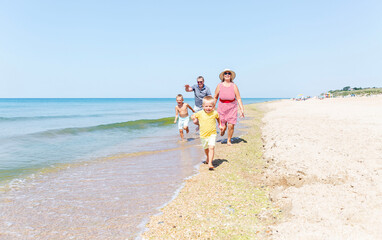 An elderly man, woman and children are running along the sandy seashore on a sunny day. Happy grandparents with grandchildren. Love and tenderness. Active holiday with family.