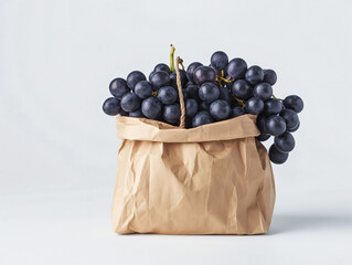 A bunch of ripe black grapes sits in a brown paper bag against a plain white background