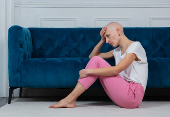 Sad young girl tired of cancer fighting sit on a floor near sofa