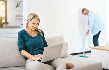 Mature, woman and home on sofa with laptop, browsing and internet search or social media break in...