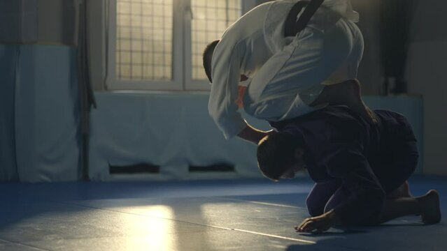 Jiu jitsu figter athlete training on sparring holding kimura lock submission on the opponents arm wearing kimono in slow-motion