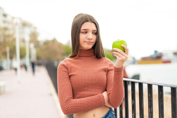 Teenager girl with an apple at outdoors with sad expression