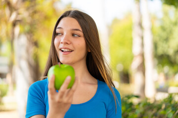 Teenager girl at outdoors holding an apple with happy expression