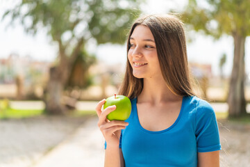 Teenager girl at outdoors with an apple and happy