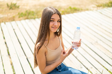 Teenager girl with a bottle of water at outdoors and pointing it