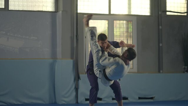 Two barefoot martial art fighters in blue and white sports uniform practicing jiu-jitsu in gym. Slow-motion shot