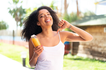 Young African American woman holding an orange juice at outdoors proud and self-satisfied