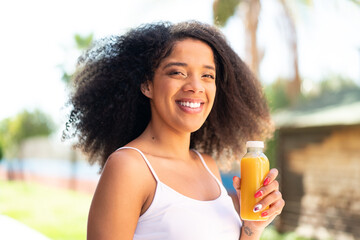 Young African American woman holding an orange juice at outdoors smiling a lot