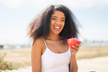 Young African American woman with an apple at outdoors smiling a lot