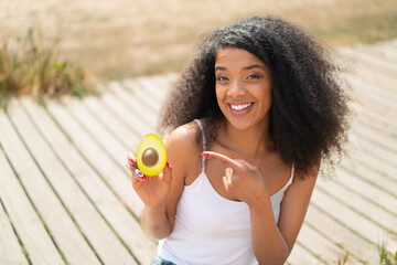 Young African American woman holding an avocado at outdoors and pointing it