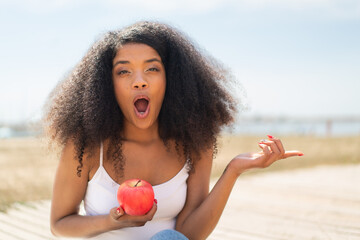Young African American woman with an apple at outdoors surprised and pointing side