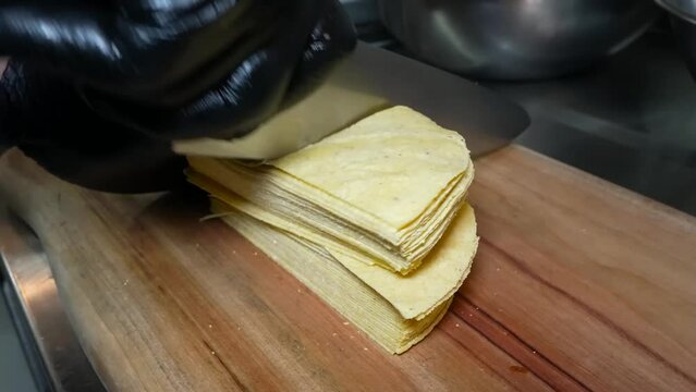 A pair of hands, protected by black gloves, expertly slicing a stack of fresh tacos into perfect quarters