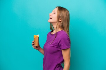 Young Russian woman catching french fries isolated on blue background laughing in lateral position