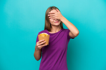 Young Russian woman catching french fries isolated on blue background covering eyes by hands. Do...