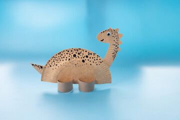 paper craft dinosaur. Made from brown paper with black spots, standing on cardboard supports. Smiling face, big round eyes. © Elena