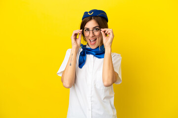 Airplane stewardess woman isolated on yellow background with glasses and surprised