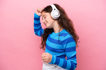 Little girl isolated on pink background listening music and dancing