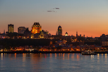 Fototapeta premium The Quebec City skyline and its illuminated buildings seen at dusk from Lévis, with the St. Lawrence River in the foreground
