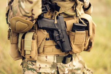 In the midst of a perilous battlefield, an army soldier stands resolute, holding a pistol ready to...