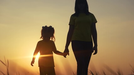 mom and daughter in the park. mom a holding her daughter hand walking in the park silhouette at...