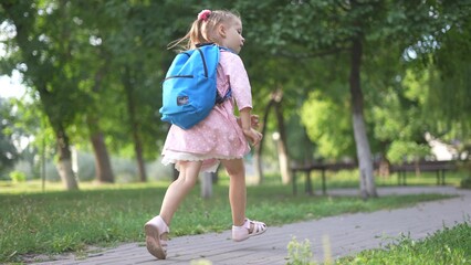 child girl with a backpack runs in the park. education learning school concept. a schoolgirl with a...