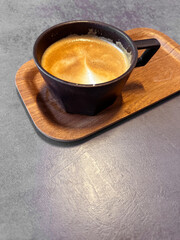 Hot Cappuccino in Stylish Black Cup on Wooden Tray on Concrete Table.