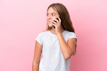 Little caucasian girl isolated on pink background keeping a conversation with the mobile phone with...