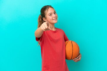 Little caucasian girl playing basketball isolated on blue background pointing front with happy...