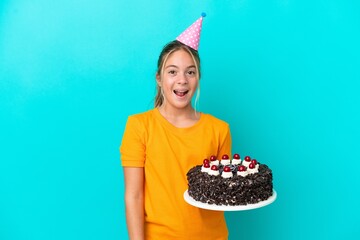 Little caucasian girl holding birthday cake isolated on blue background with surprise facial...
