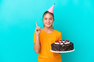 Little caucasian girl holding birthday cake isolated on blue background pointing up a great idea