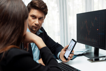 Focusing on phone with discussing dynamic stock market in two business traders online website compare with pc screens in real time currency rate investment on risk data at modern office. Postulate.