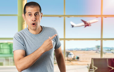 Fototapeta premium Handsome man wearing casual grey shirt at airport.Surprised pointing with finger to the side, open mouth amazed expression.