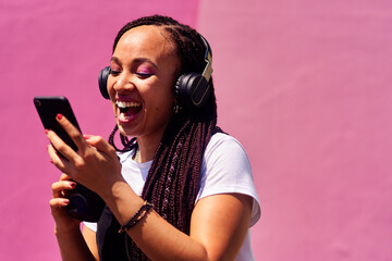Woman, headphones and happy music for podcast in the city, pink wall background and video call on...