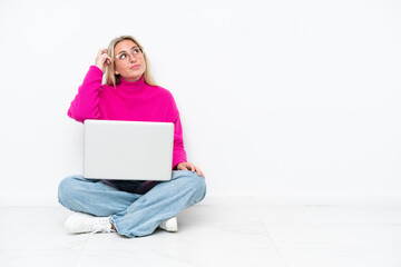 Fototapeta premium Young caucasian woman with laptop sitting on the floor having doubts and with confuse face expression