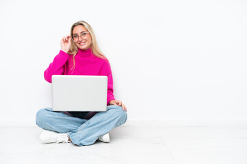 Young caucasian woman with laptop sitting on the floor with glasses and happy