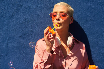 Young, woman and blowing bubbles against wall for fashion or wellness, cool with heart sunglasses...