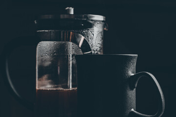 French press filled with coffee and an empty mug in front, highlighting brewing process and warmth.