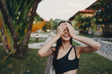 Woman standing in front of palm tree, covering eyes with hands and feeling the warmth of the sun
