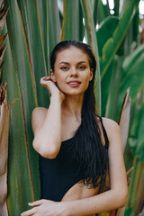 Exotic beach beauty attractive young woman in black swimsuit posing by tropical palm trees and lush...