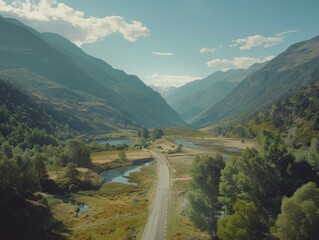 Aerial view of a winding mountain road meandering through a lush valley with trees, river, and sunlight.