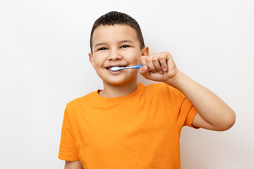 A little boy in an orange T-shirt carefully brushes his teeth.