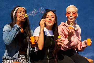 Blowing bubbles, women and fun at wall with urban fashion, streetwear and nostalgia in city. Girl...