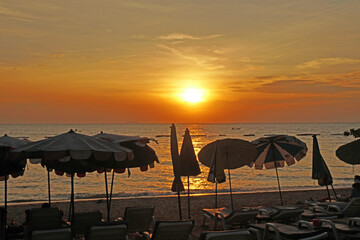 Landscape Tranquil scene of big red sun and yellow sky sunset over the sea and silhouette umbrella beach chair at pattaya Thailand.