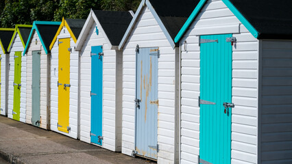 A row of colourful seaside beach huts with brightly painted doors and trim at popular beach holiday...