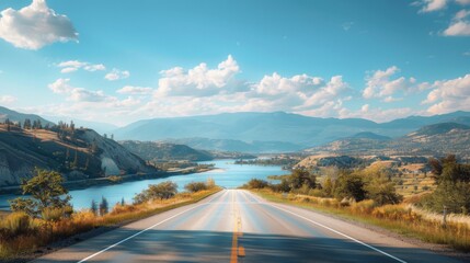 Empty road stretching towards the horizon with clear blue skies and scenic mountains by a lake.