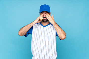 Young man playing baseball over isolated blue background covering eyes by hands
