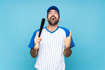 Young man playing baseball over isolated blue background surprised and pointing up