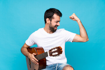 Young man with guitar over isolated blue background celebrating a victory