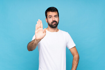 Young man with beard  over isolated blue background making stop gesture