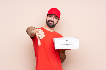Young man holding a pizza over isolated background showing thumb down with negative expression